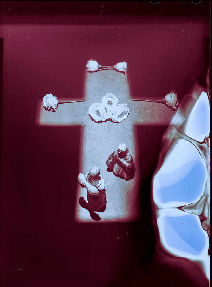 A photograph of a cross made of light, with flowers laid on like a tomb, and Mary Magdalene and an angel inside the tomb.